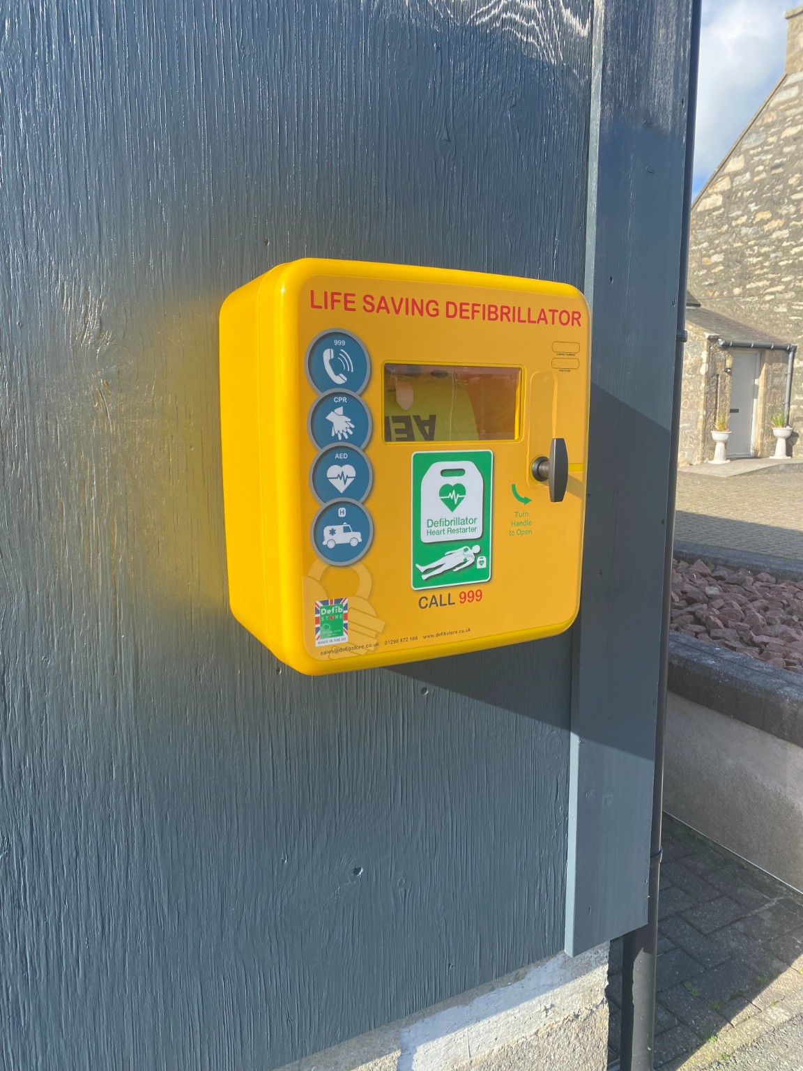 Close-up of the bright yellow defibrillator cabinet with its call 999 signage